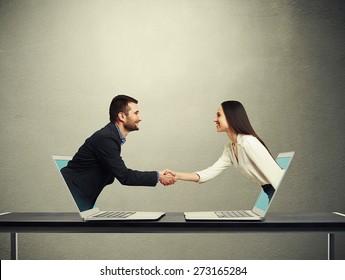 smiley businessman and businesswoman come out from laptop, shaking hands and looking at each other over dark grey background - Powered by Shutterstock