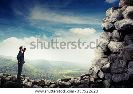 smiley businessman holding his hand near brow and looking up at stone mountain
