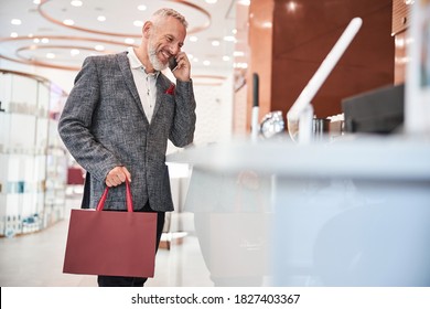 Smiley Elderly Man Making A Phonecall And Holding A Dark-red Gift Bag