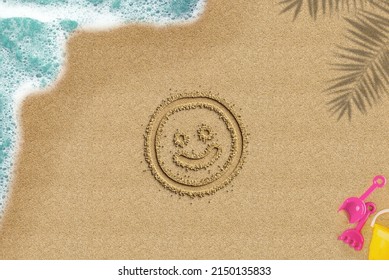 Smiley Face Drawn On Sandy Beach, Travel And Holiday Concept, Emoji Idea, Palm Shadow And Sea Wave And Toys Composition, Top View Of Sand Beach