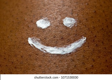 Smiley Face Drawn With Sun Cream Or Sunscreen Lotion On Dark Brown African American Skin Texture For Summer Skin Care And Health Concept.