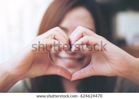 A smiley face woman making heart hand sign over her face with feeling love