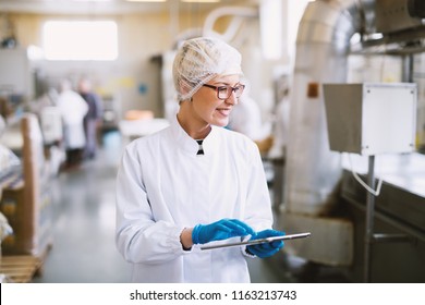 Smiley female worker in sterile clothes using tablet and checking how production line is working. - Powered by Shutterstock