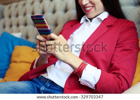 smiley young woman sitting on sofa and chatting on smartphone