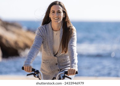 Smililng young woman, looking at camera, and riding a bicycle by the sea - Powered by Shutterstock