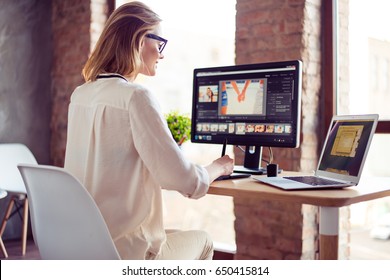 Smilimg blond girl is working at home on computer, using her laptop also. She is a graphic designer. Retouch is her hobby, she is self employed freelancer - Shutterstock ID 650415814