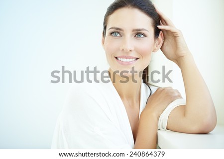 Smiling 30 year old woman at the window. Fresh light blue background.
