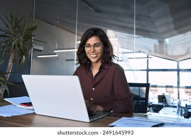 Smiling 30s latin hispanic middle-aged business woman working on laptop computer in modern office. Indian young businesswoman professional employee using pc doing online banking analysing at workplace - Powered by Shutterstock