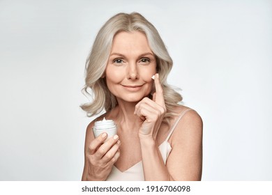 Smiling 50s Middle Aged Mature Woman Putting Tightening Facial Cream On Face Looking At Camera. Anti Age Healthy Dry Skin Care Beauty Therapy Concept, Skincare Rejuvenation Treatment Against Wrinkles.