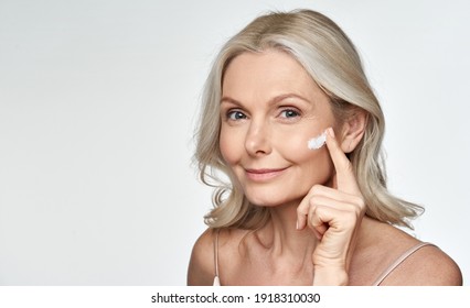 Smiling 50s Middle Aged Mature Older Woman Applying Facial Cream On Face Looking At Camera Isolated On White Background. Anti Age Healthy Dry Skin Care Beauty Therapy Concept, Old Skincare Treatment