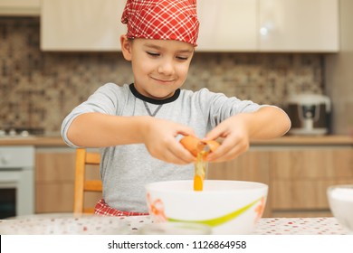 Smiling 7 year old boy helping in the kitchen, breaking eggs into large bowl. - Powered by Shutterstock