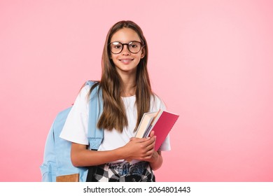 Smiling active excellent best student schoolgirl holding books and copybooks going to school wearing glasses and bag isolated in pink background