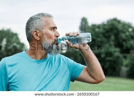 Smiling active mature mid aged coman jogging exercising and having fun and l taking a break drinking water  in the park