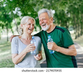 Smiling active senior couple holding water bottles  drinking    jogging together in the park
