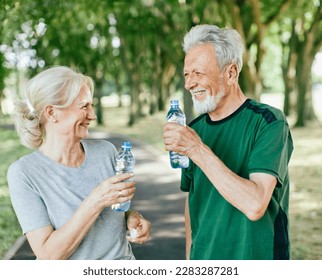 Smiling active senior couple holding water bottles, drinking and  jogging together in the park - Powered by Shutterstock
