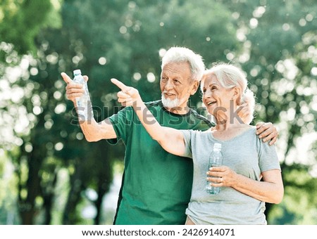 Smiling active senior couple holding water bottles, drinking and  jogging together in the park