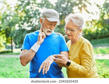 Smiling active senior couple jogging exercising and having fun and laughing together taking a break in the park, senior athletes checking their er heart rate with smartwatch - Shutterstock ID 2343265435