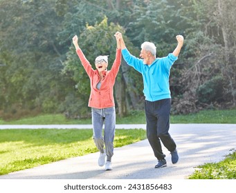 Smiling active senior couple jogging exercising and having fun and celebrating success rasing hands together taking a break in the park - Powered by Shutterstock