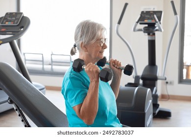 Smiling and active senior woman doing exercises with dumbells in gym area. Sport, health, gym, wellness concept - Powered by Shutterstock