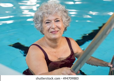 Smiling Active Senior Woman Entering In A Swimming Pool. Smiling Old Woman Looking At Camera Before The Water Aerobics Lesson. Happy Mature Woman Ready To Swim.