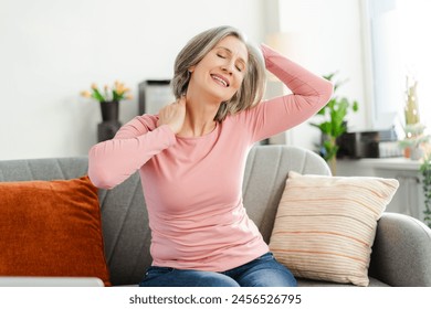 Smiling active senior woman stretching head, doing exercises sitting on comfortable sofa relaxing at home. Happy female, freelancer taking a break, resting. Natural beauty, healthy lifestyle concept  - Powered by Shutterstock