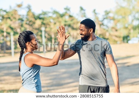 Smiling active young couple jogging exercising and having fun and laughing together taking a break after walking and running in the park, high five exchange