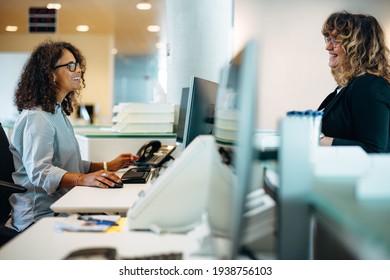 Smiling Administrator Talking With A Woman Standing At Reception Desk. Woman Visiting Municipal Office For Work And Talking With The Receptionist.