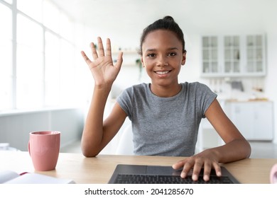 Smiling Adolescent Afro American Girl Student Study At Home With Laptop, Calling Online And Waving Hand To Webcam Indoor. Social Distance, Remote Education, Meeting With Teacher During Covid-19 Virus