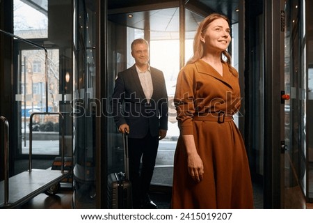 Smiling adult caucasian couple with suitcases entering to hotel lobby at daytime