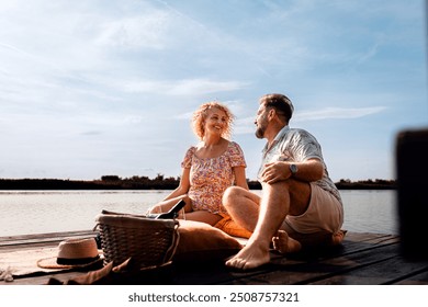 Smiling adult couple sitting by the lake on a pier drinking wine during sunset. - Powered by Shutterstock