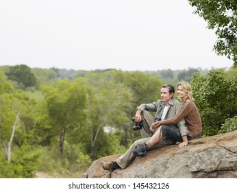 Smiling adult couple sitting on rock and enjoying the view - Powered by Shutterstock