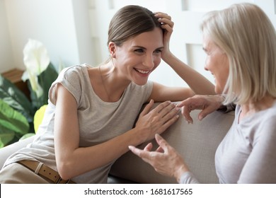 Smiling Adult Daughter Listening To Older Mother, Talking, Sitting On Cozy Couch At Home, Happy Young Woman And Mature Mum Or Grandmother Chatting, Having Fun, Sharing News, Two Generations