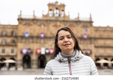 Smiling Adult Female Tourist Enjoying Walking In Ancient Spanish City Of Salamanca On Spring Day, Posing In Central Plaza Mayor..