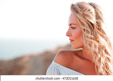 Smiling Adult Girl With Curly Blonde Hair Looking Away Over Sea Background. Side View. Summer Portrait. 20s.