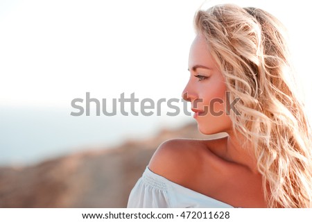Smiling adult girl with curly blonde hair looking away over sea background. Side view. Summer portrait. 20s.
