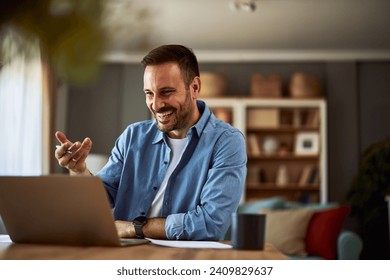 A smiling adult male online teacher engaging his students in an online class using an online platform on his laptop.