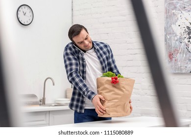 Smiling Adult Man Carrying Grocery Store Bag And Talking By Phone At Kitchen