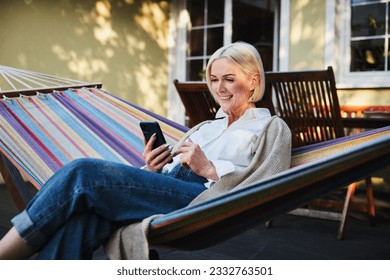 Smiling adult woman in hammock using mobile phone during sunny afternoon in house terrace - Powered by Shutterstock