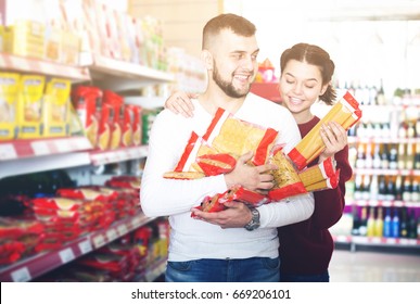 Smiling Adults Reading Lable Of Pasta At Supermarket