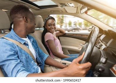 Smiling African Amerfican Man And Woman Sitting In The Luxury Car, Cheerfully Looking At Each Other, Having Conversation, Happy Black Lovers Having Weekend Trip Together, Driving Auto