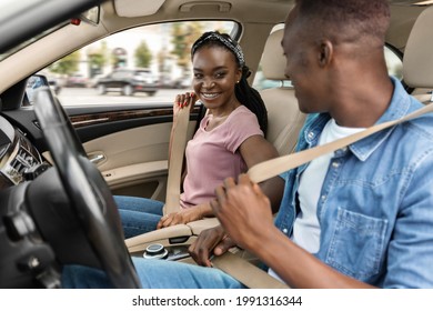 Smiling African Amerfican Man And Woman Fastening Seat Belts After Get In The Luxury Car, Cheerfully Looking At Each Other, Happy Black Lovers Having Weekend Trip Together, Driving Auto