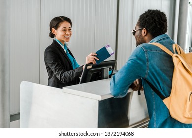 smiling african american airport worker giving passport and air ticket to tourist with backpack - Powered by Shutterstock