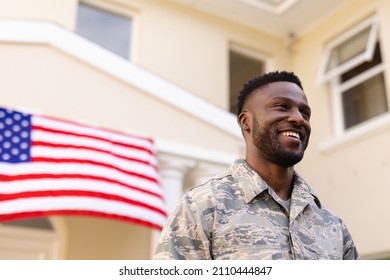 Smiling African American Army Man Looking Away Against House With America Flag. Patriotism And Identity, Unaltered.