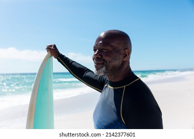 Smiling african american bald senior man holding surfboard looking away at beach on sunny day. unaltered, active lifestyle, aquatic sport and holiday concept. - Powered by Shutterstock