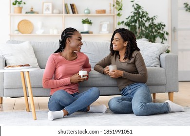 Smiling african american besties young women having conversation while drinking coffee at home, sitting by couch on floor at living room, copy space. Friendship, sisterhood concept - Powered by Shutterstock