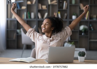 Smiling African American Biracial Business Woman Manager Worker Raising Up Arms, Stretching Back, Relaxing After Finishing Hardworking Day, Meeting Deadline, Dreaming Visualizing In Modern Home Office