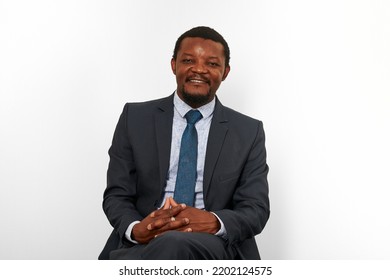 Smiling African American Black Man In Business Suit Sitting On Chair Isolated White Background. Happy Black Executive Businessman, Chief Executive Officer Satisfied Successful Interview With Applicant