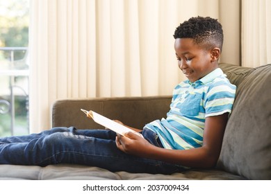 Smiling african american boy reading book and sitting on couch in living room. spending time alone at home. - Powered by Shutterstock