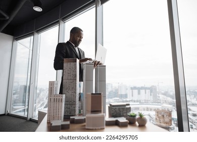 Smiling african american business man real estate agents in black stylish formal suit standing with laptopnear 3d model skyscrapers of city architecture design at office with panoramic city view. - Powered by Shutterstock - Get 15% off with code: PIKWIZARD15