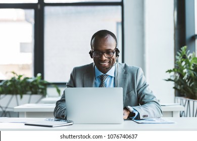 smiling african american businessman in eyeglasses and headset using laptop in office - Shutterstock ID 1076740637